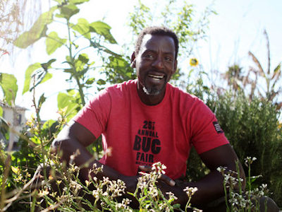 Ron Finley in a red shirt in the middle of a garden, smiling