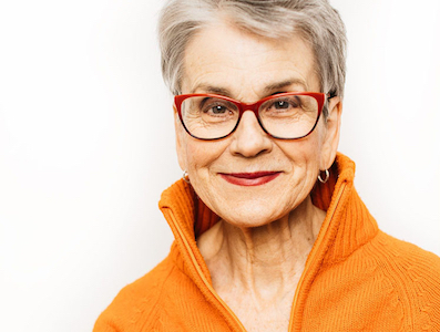 Frances Moore Lappe in an orange shirt and red glasses, smiling at the camera.