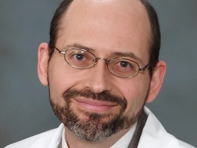 headshot of Michael Greger, M.D. in a white coat with glasses, smiling